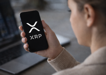 Person holding a smartphone displaying the XRP cryptocurrency logo while checking digital asset markets.