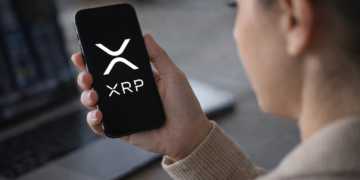 Person holding a smartphone displaying the XRP cryptocurrency logo while checking digital asset markets.