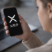 Person holding a smartphone displaying the XRP cryptocurrency logo while checking digital asset markets.