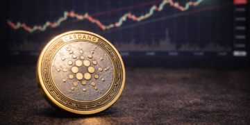 A Cardano (ADA) cryptocurrency token placed on a table with a blurred upward-trending market chart in the background.