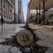 Bitcoin coin lodged in a deep crack between Wall Street and a rundown gas station street, symbolizing fragile markets as record highs clash with collapsing consumer confidence